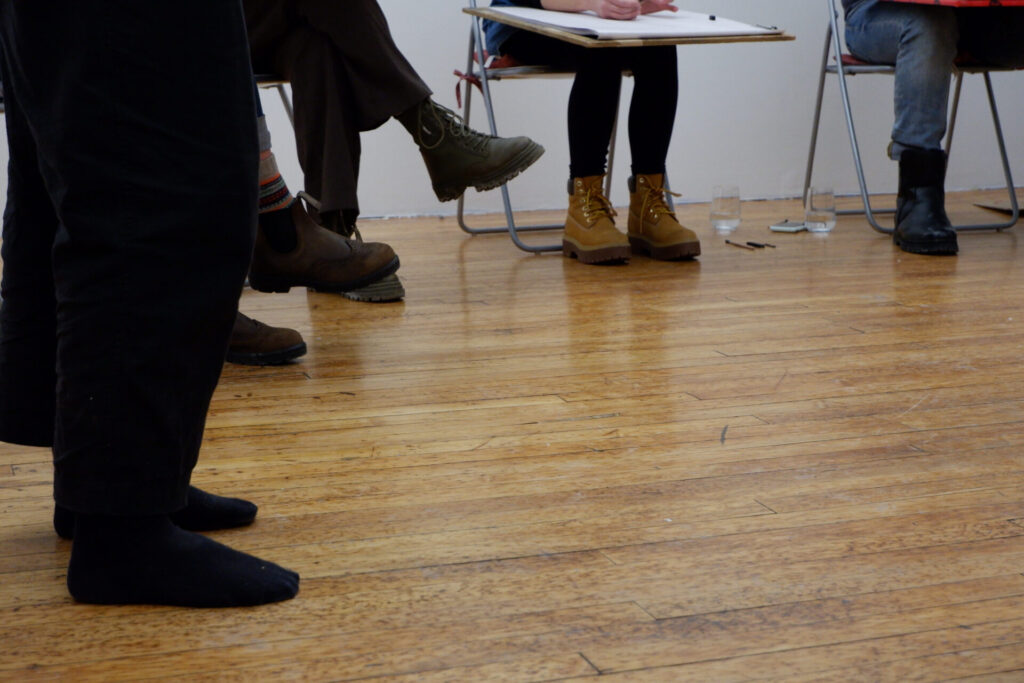 Participants sitting in a circle with drawing boards during the workshop, view of the wooden floor.