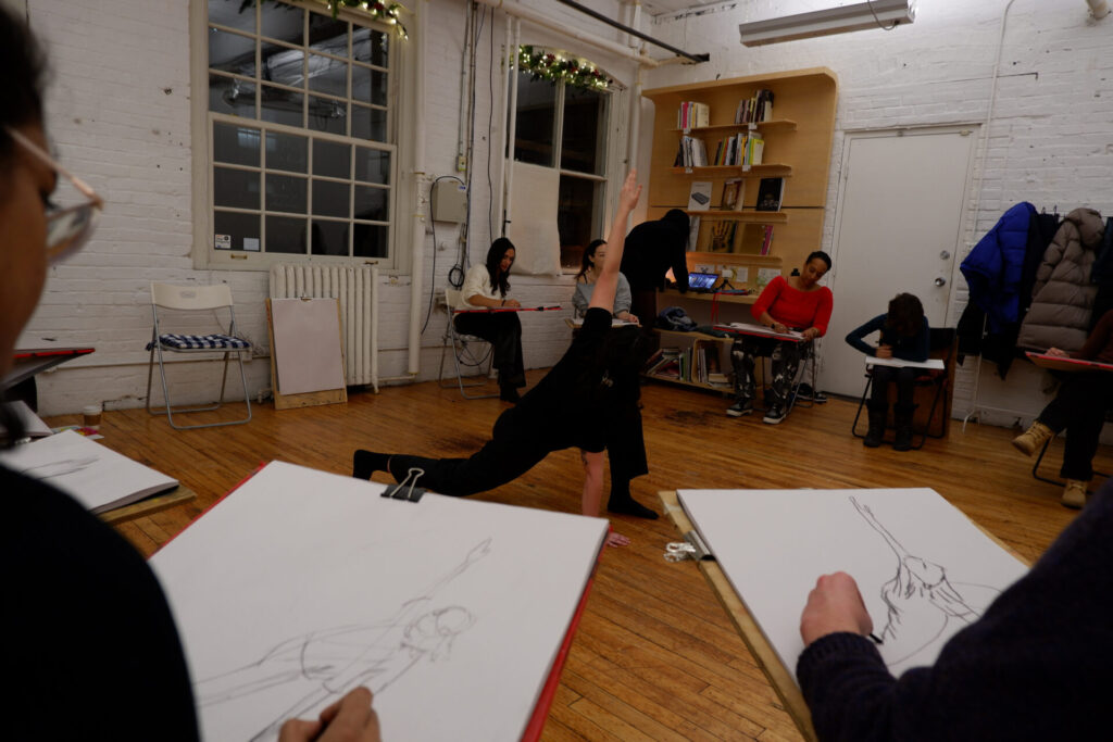 Life drawing session in the art studio, participants sketching a pose on the floor.