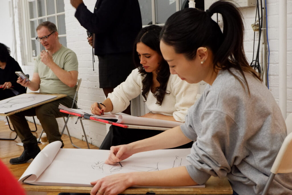 Two focused participants drawing on large sheets attached to drawing boards during the workshop.