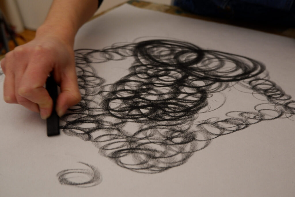 Hand drawing charcoal circles on a white sheet of paper.