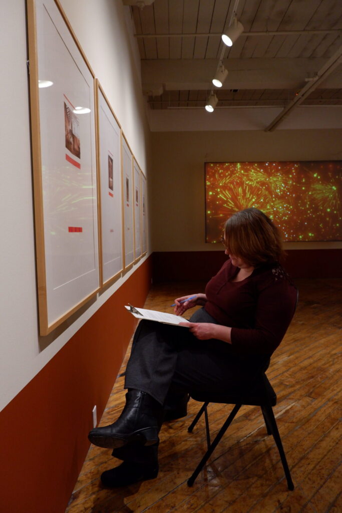 A participant writing their observations in a notebook in front of an exhibition during the workshop.