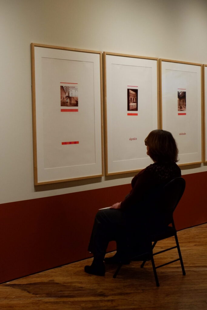 A seated participant observes framed artworks hanging on the wall in the gallery.