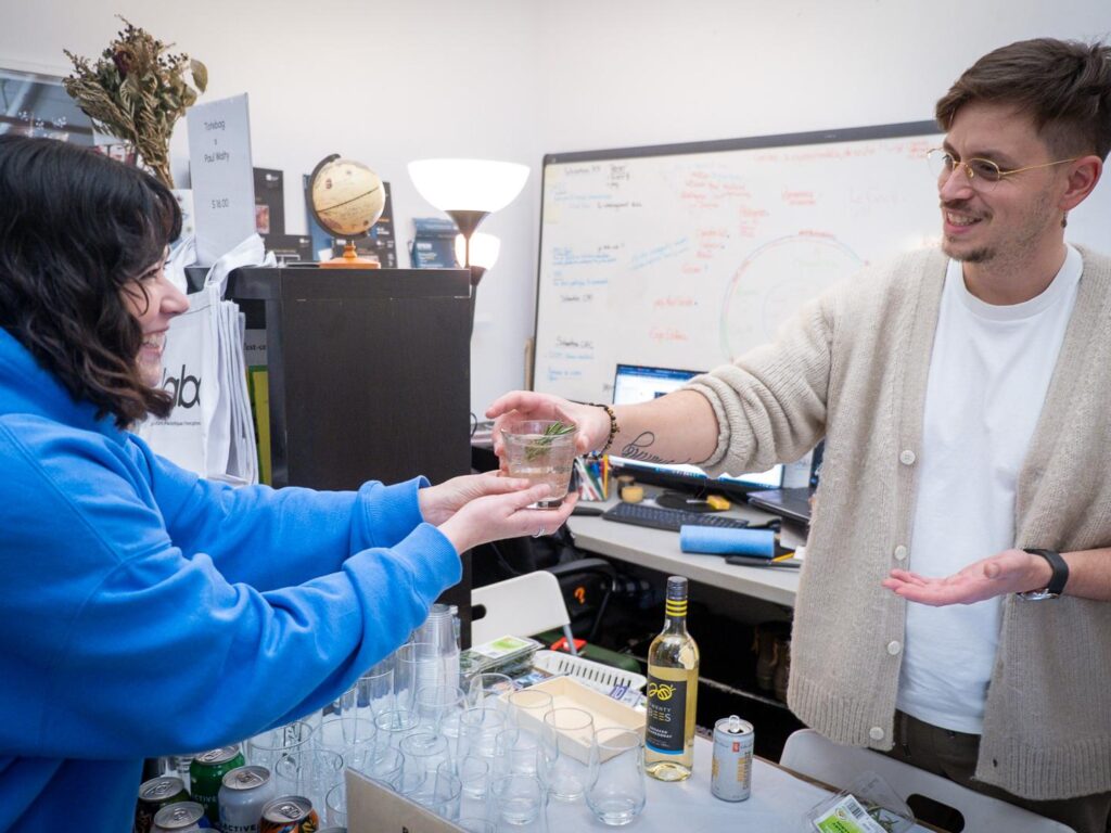 Deux personnes échangent un verre lors d’un événement au studio, entourées de verres et de matériel sur une table.
