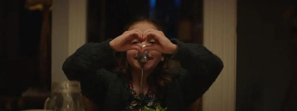 A child forms a heart with her hands in front of her face, in a warm scene from the film Rêver en néon.